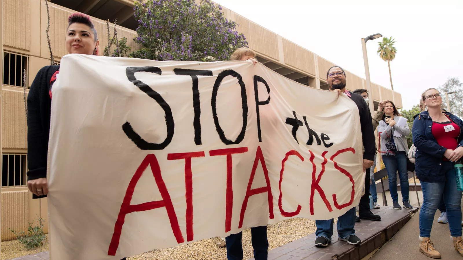 Picture of two teachers holding a banner that says "Stop the Attacks"